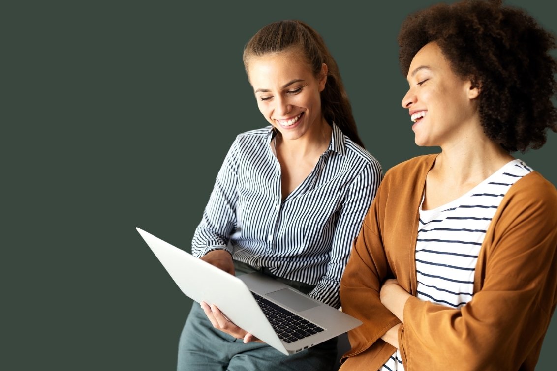 Two business women smiling at laptop.