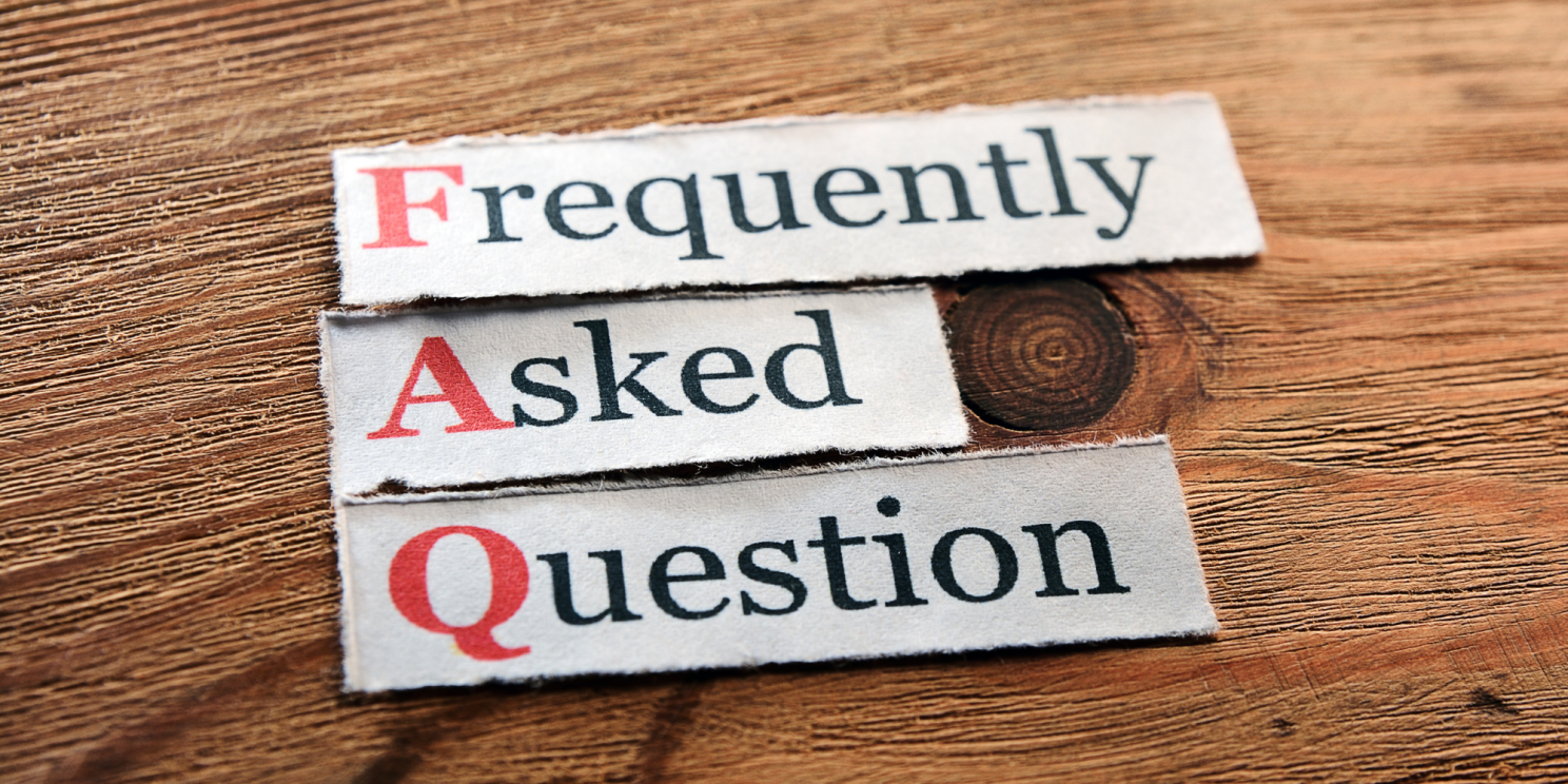 The photo shows a close-up shot of a wooden table on which three pieces of paper are lying. Each piece has one word printed on it. Starting from the top, the words read: "Frequently", "Asked", "Question".