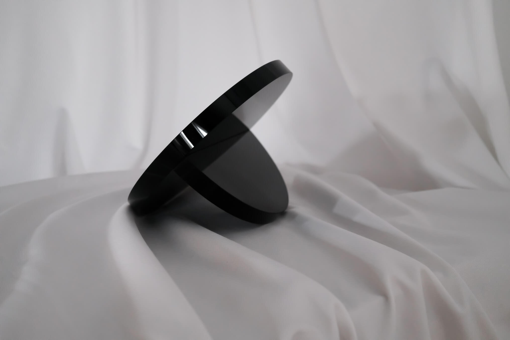 a side view of a hand mirror, a black disc of glass with a a half circle of the same material perpendicularly mounted to the back, holding it up at an angle.