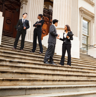 Four well dressed professionals in discussion on the exterior steps of a building.