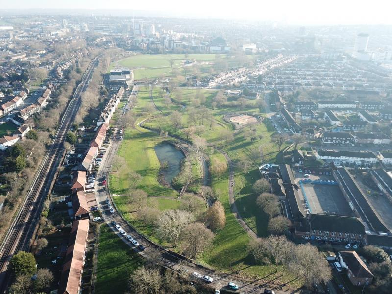 An aerial view of a large London park, with a central lake and housing surrounding every side.
