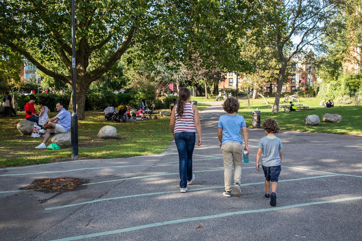 Three children walking through a busy, sunny park.