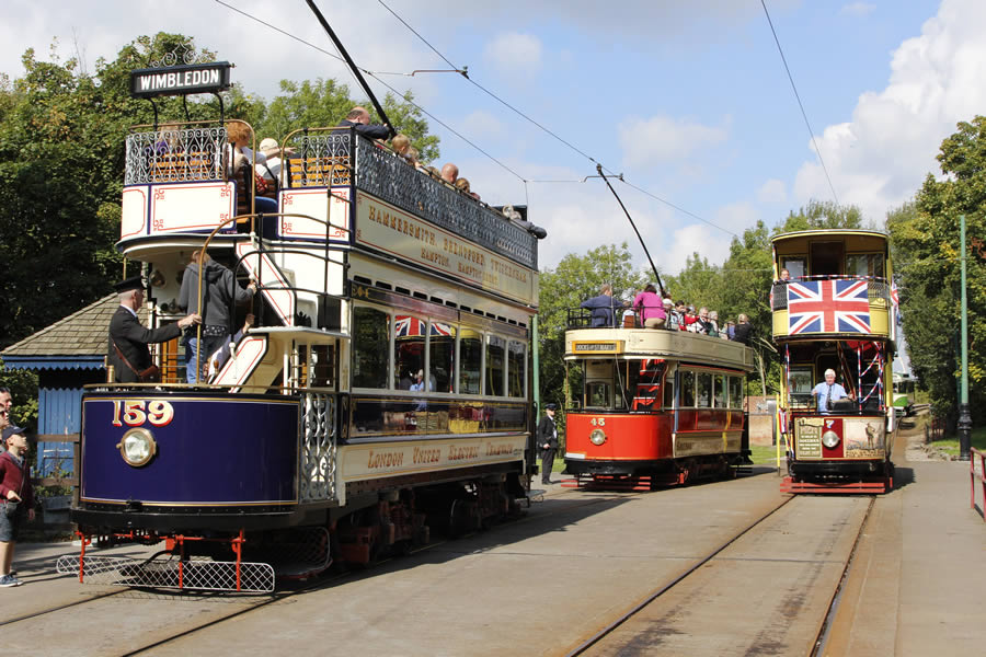 Three old-fashioned British trams filled with people on tramlines