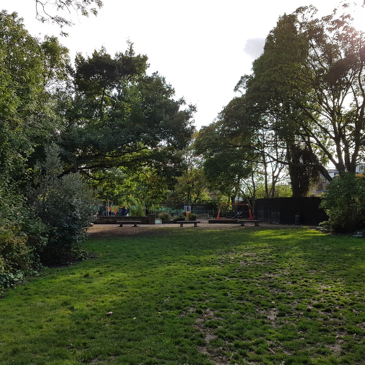 The image shows a green park with a small children's playground at the back.