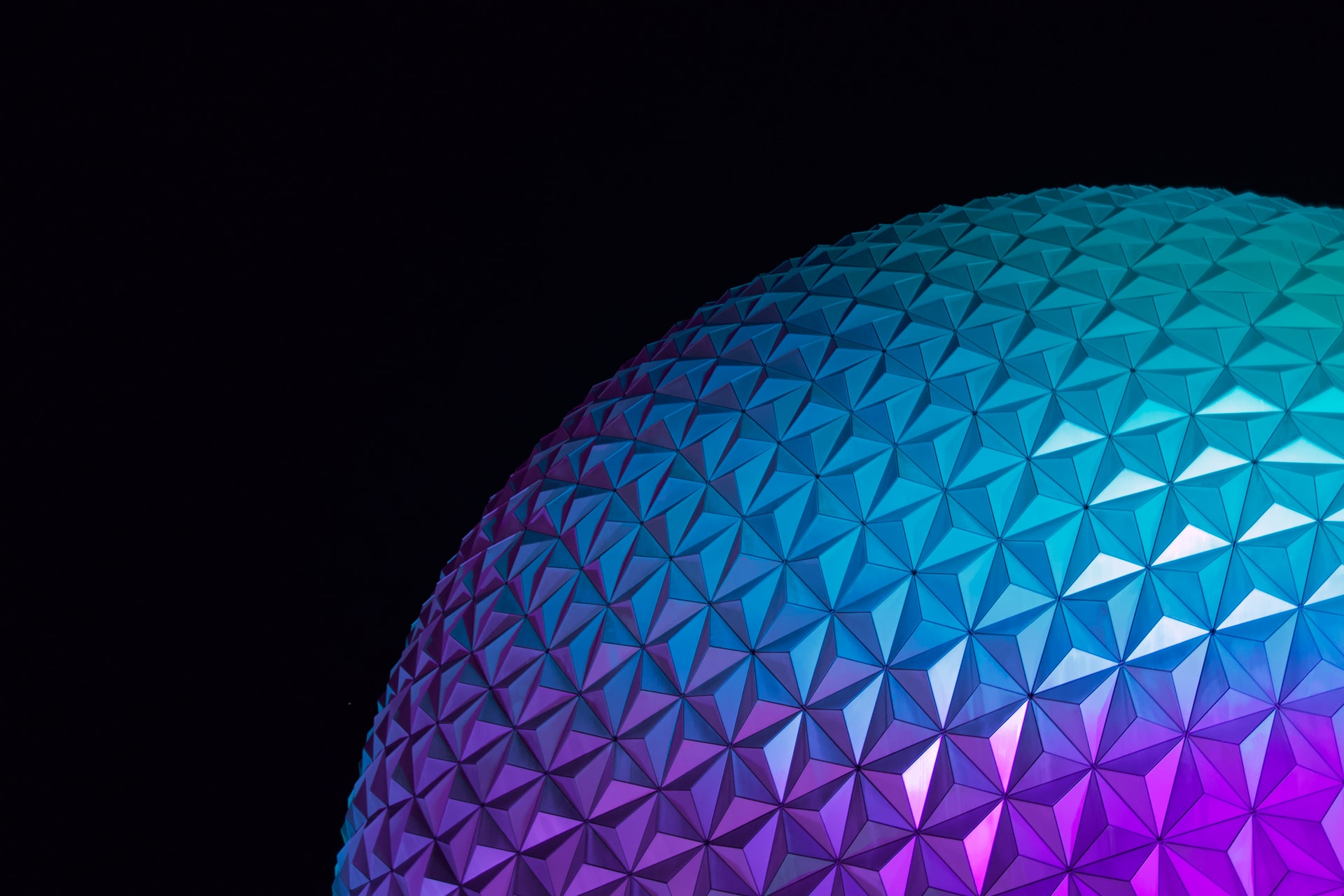 Part of a globe made of geometric patterns lit up in blue and purple against a dark backdrop.