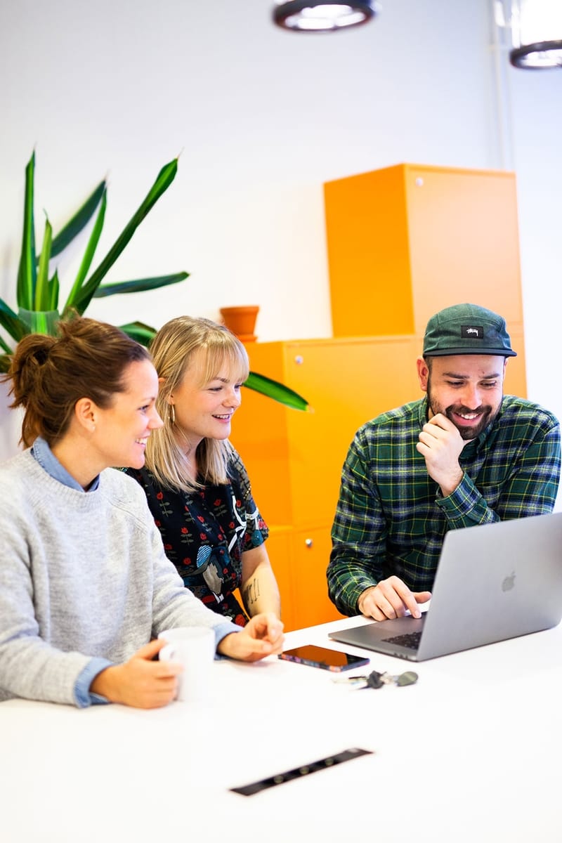 two women and one man working together at a desk staring on a computer