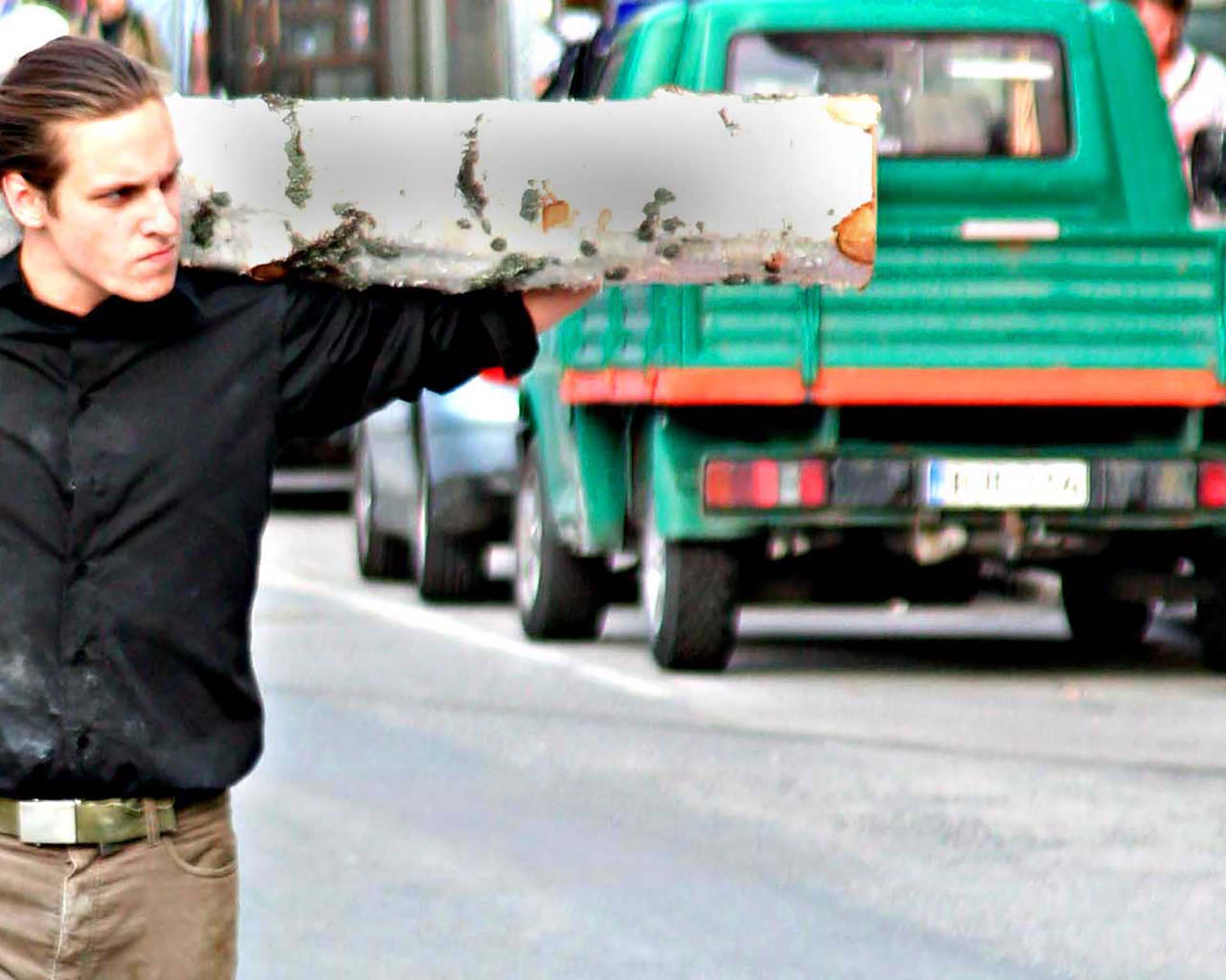 A guy walking on a city road with a large piece of wood on the shoulders