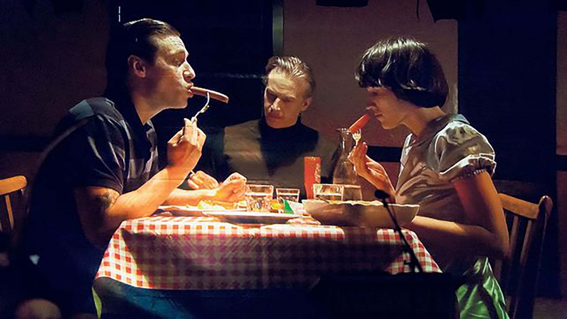 A family sitting with a table, two of them is eating sausage