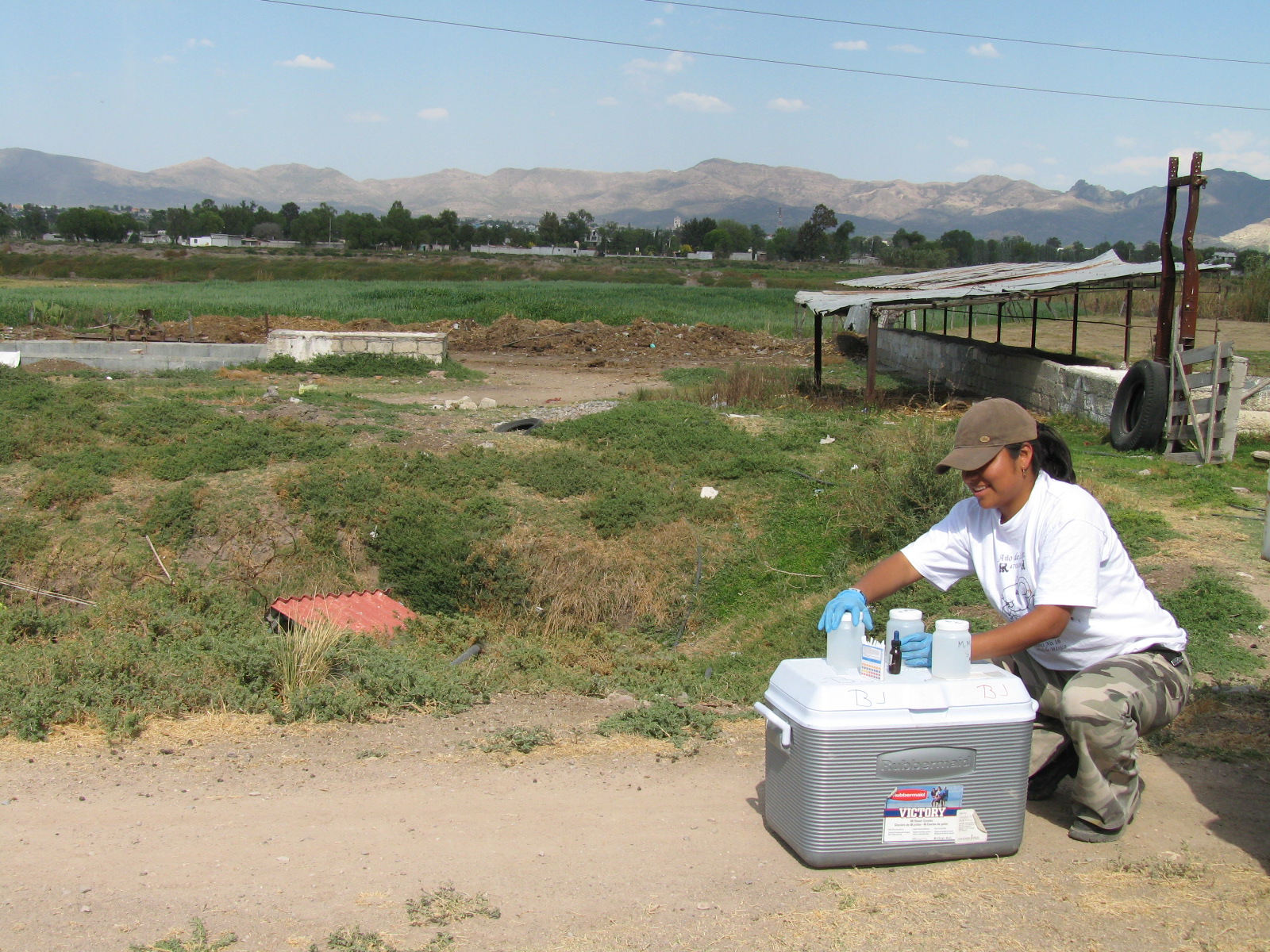 Woman testing water on top of a cooler in field.