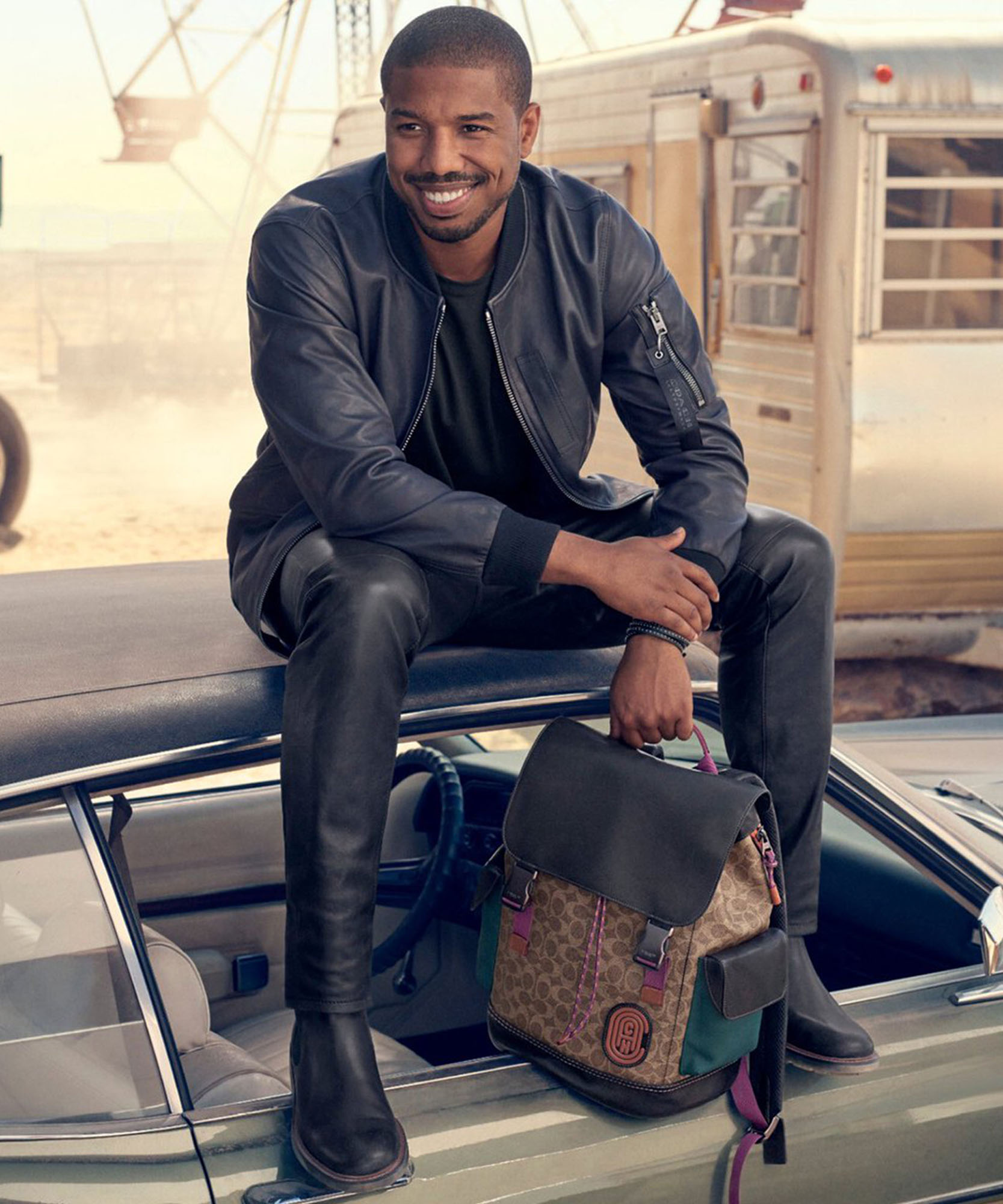 a photo of male model sitting on car holding backpack