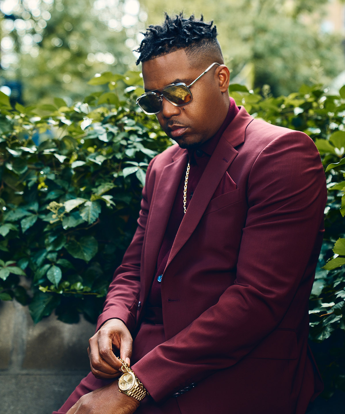 nas wearing an all burgundy suit fixing his gold bracelet that on top of his gold watch