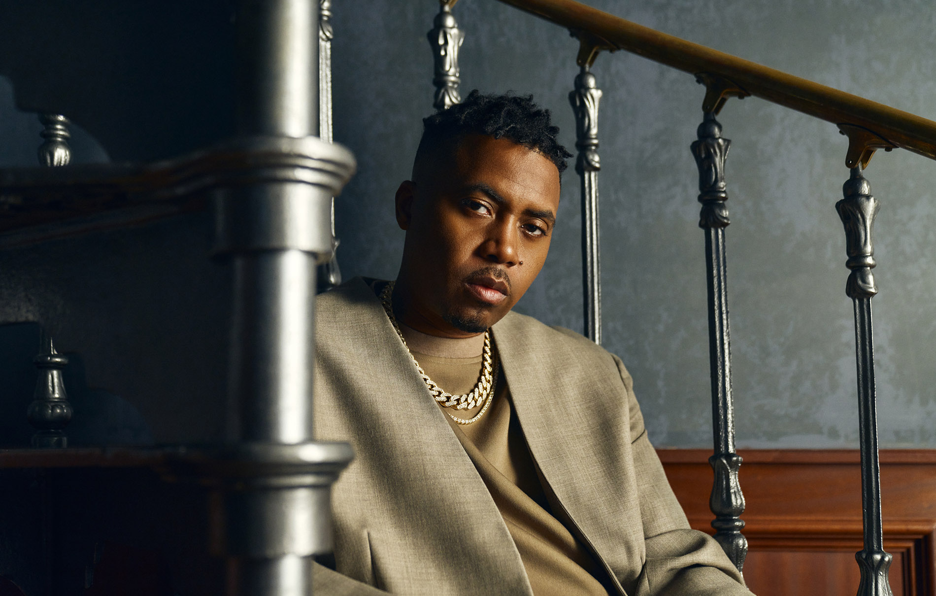up close view of nas sitting on stairs with a all tan suit wearing two gold chains