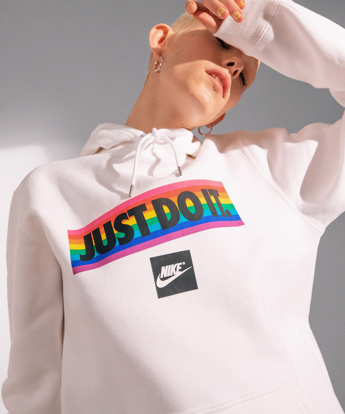 up close view of model wearing a nike just do it multi colored hoodie holding here hand in front of her eyes as if she is blocking the sun
