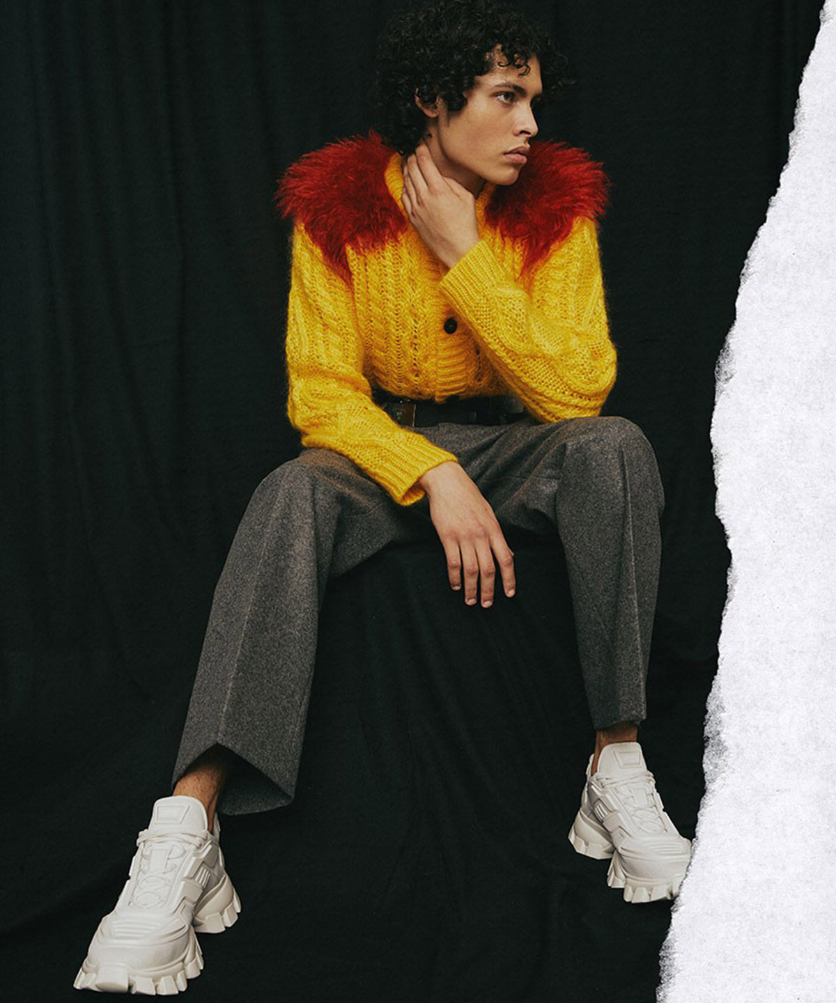 photo of model sitting down with a yellow sweater white show and a black curtain background