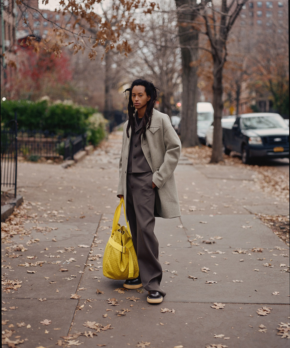 model holding yellow bag on a city sidewalk with many leaves on the ground