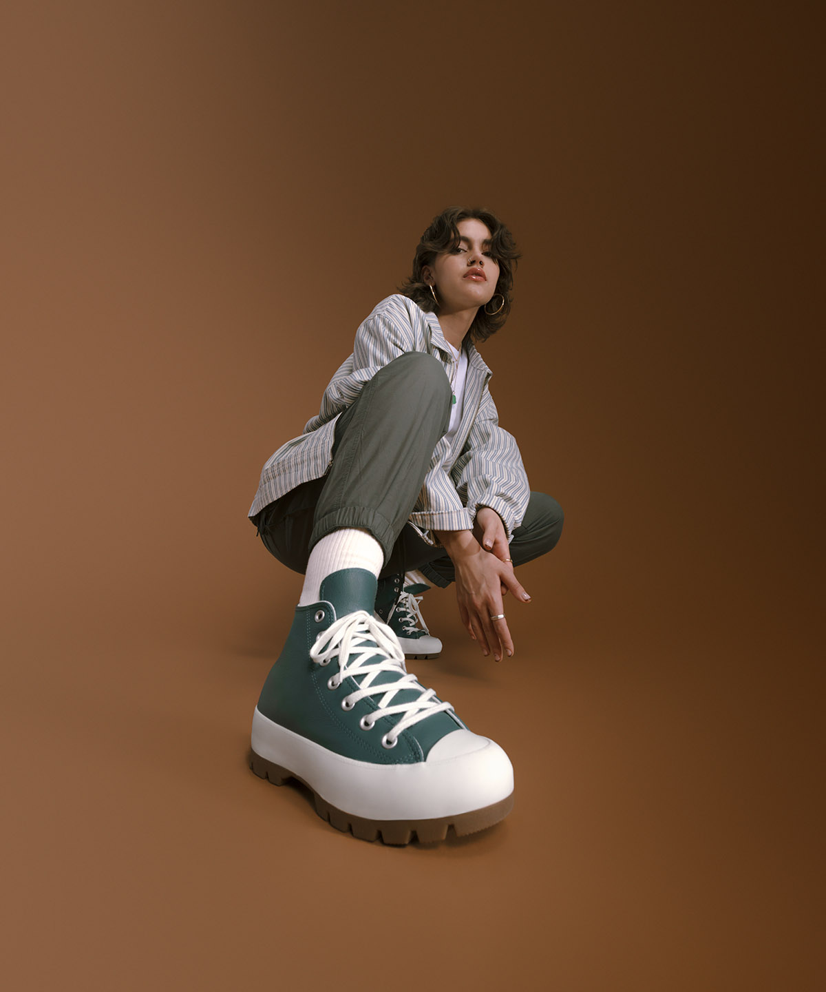 women model kneeled down showing her converse shoe with a white background