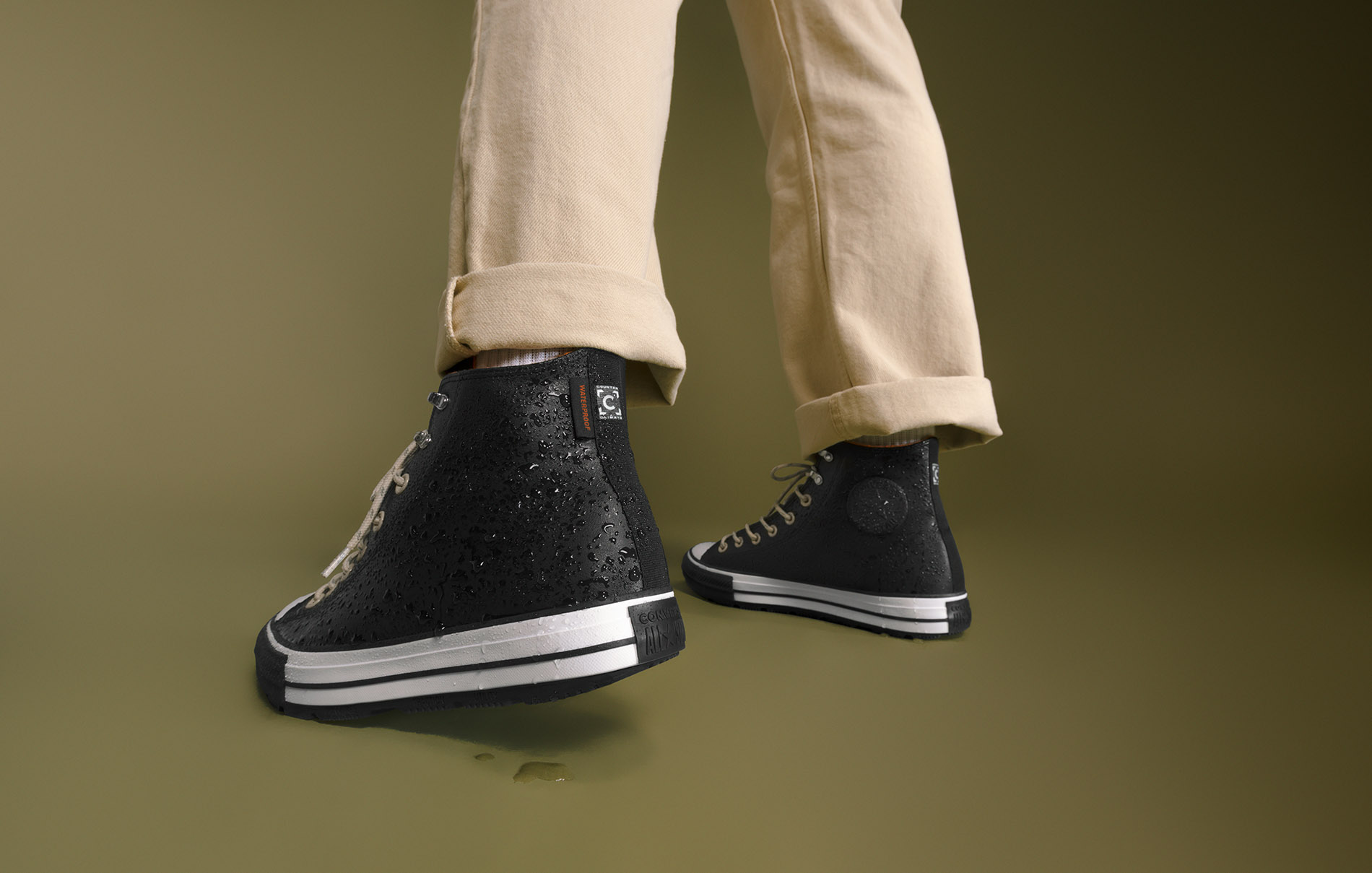A view of black converse shoes cuffed tan jeans with a green background