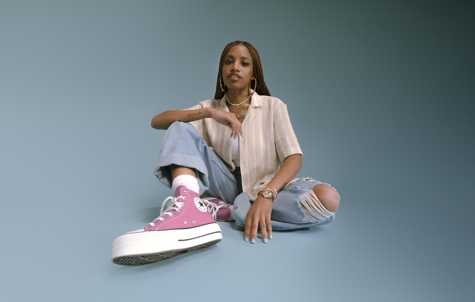 model sitting down wearing pink converse with a blue background