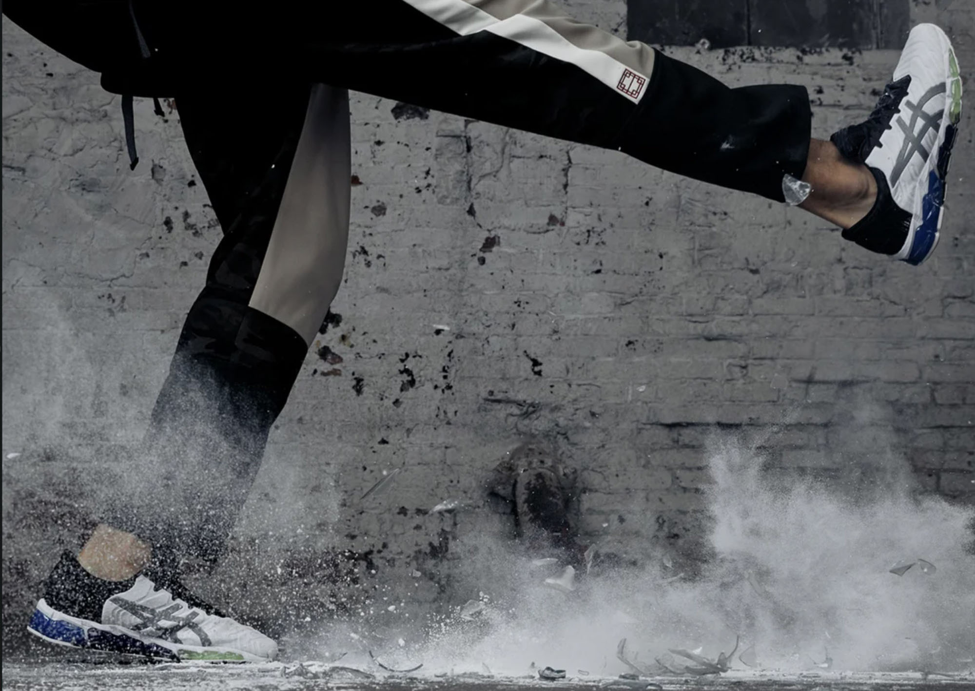man kicking rocks in an industrial setting with a exposed brick background showing only legs with black athletic wear