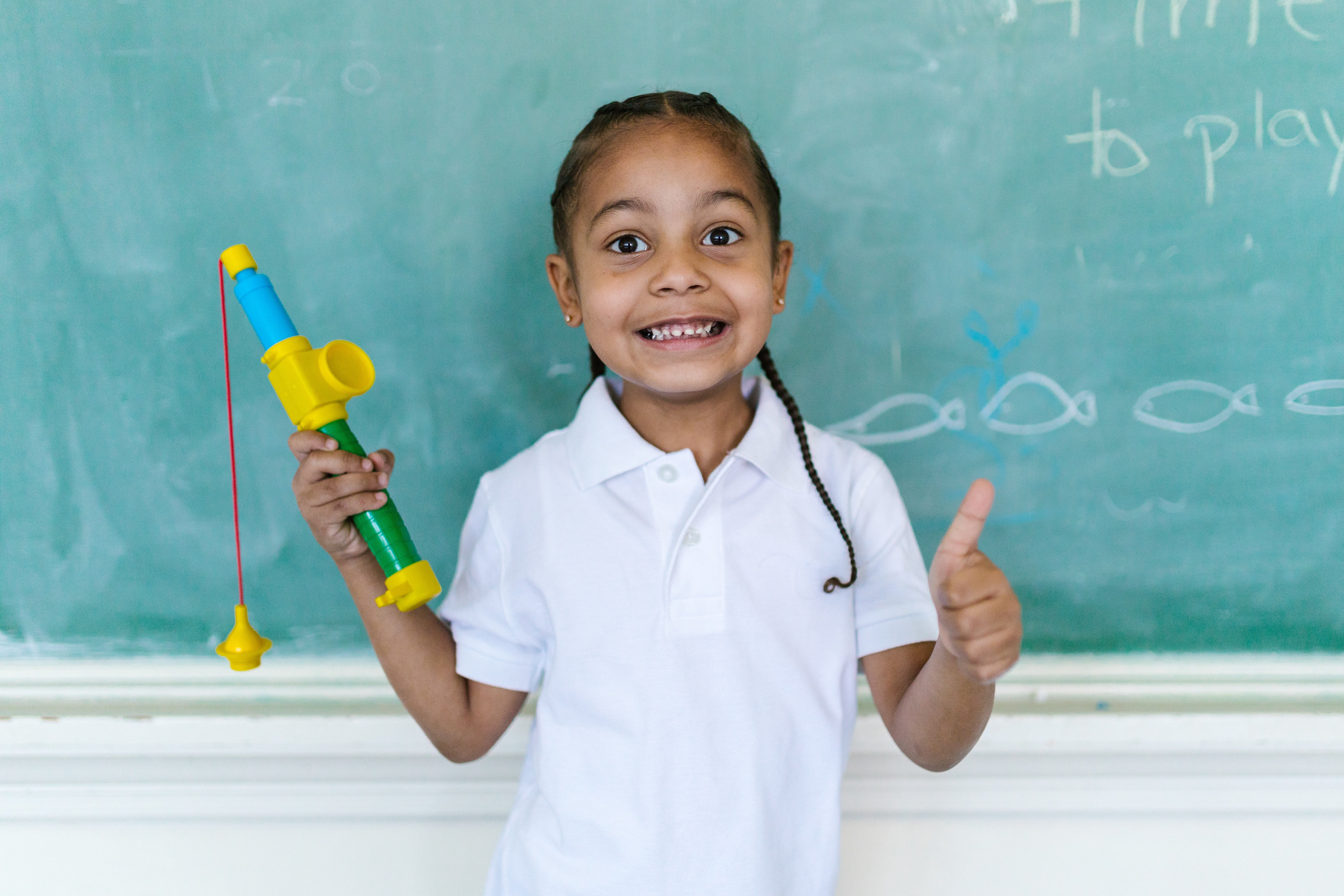 Child stands in front of chalkboard holding a block creation, smiling, and giving a thumbs up.