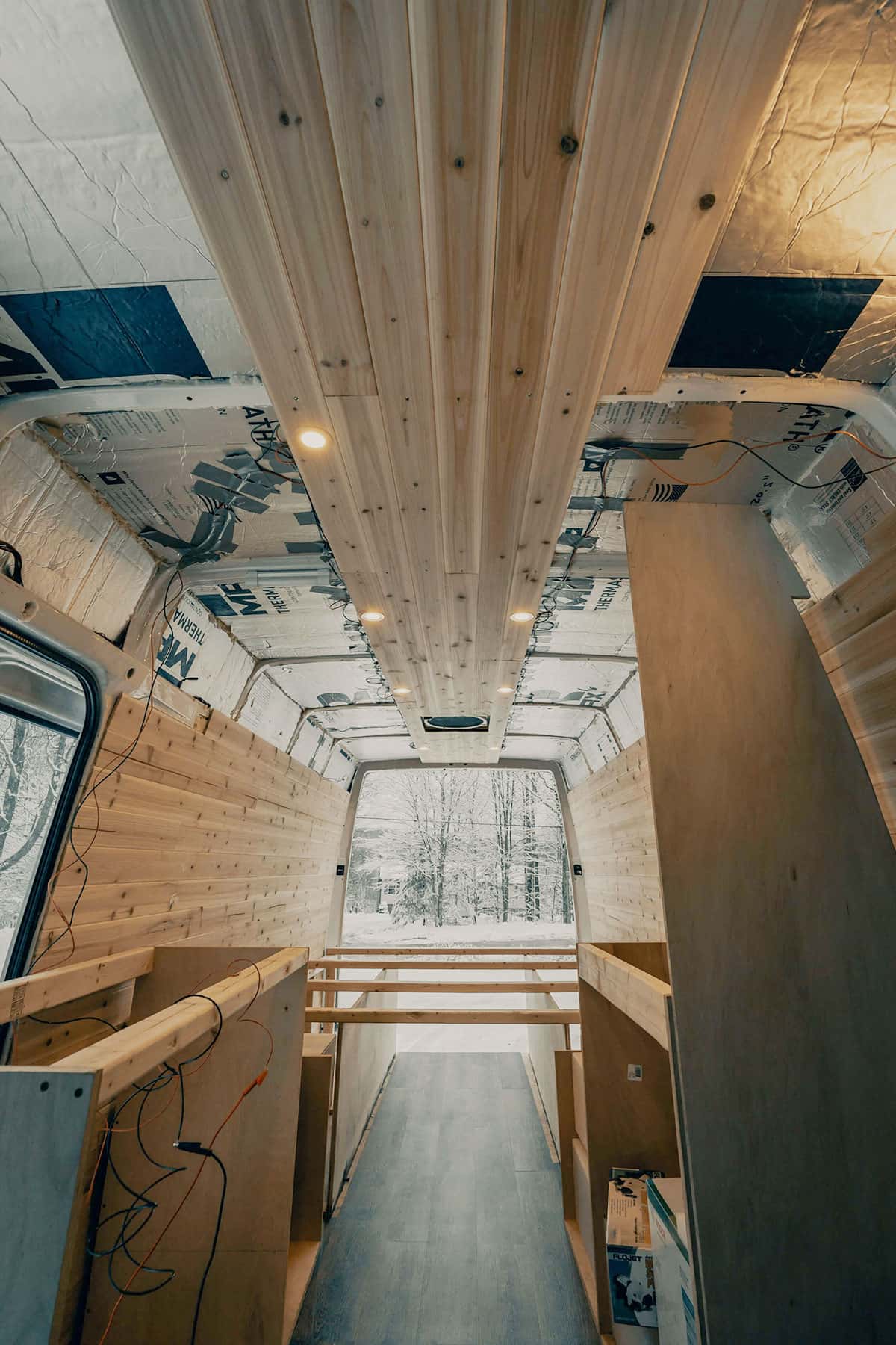 Innenraum eines teilweise selbstausgebauten Transporters; Holzpaneele und Deckenleuchten, Bettgestell