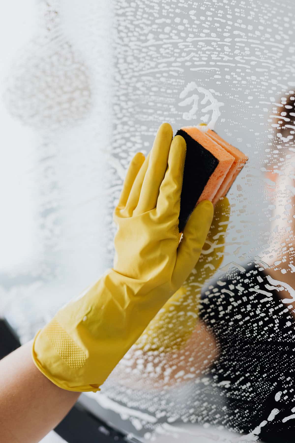 Eine Hand mit gelbem Putzhandschuh und Schwamm putzt einen Spiegel