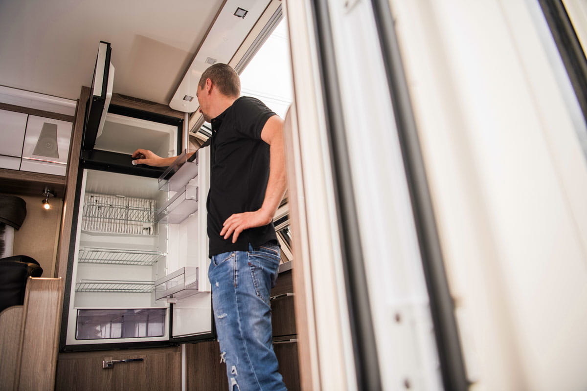 Mann steht vor geöffnetem Wohnmobil-Kühlschrank und inspiziert ihn