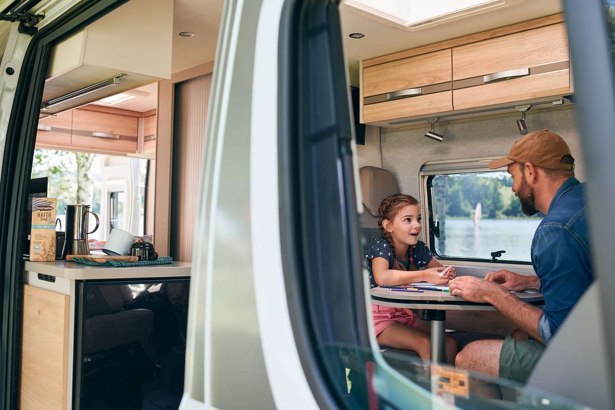 Vater und Tochter sitzen gemeinsam am Tisch im Campingbus und malen