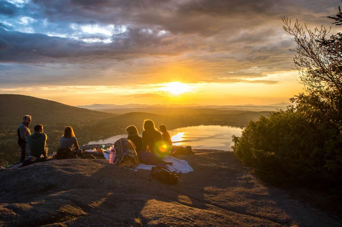 Freundesgruppe genießt bei Sonnenuntergang den Blick auf ein Maar in der Eifel