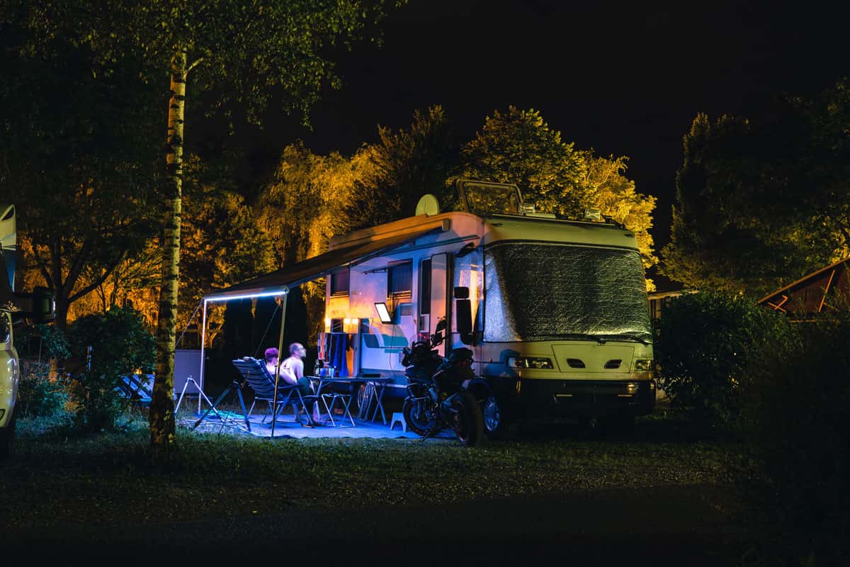 Pärchen schaut Nachts fernsehen auf einem Fernseher der am Wohnmobil hängt