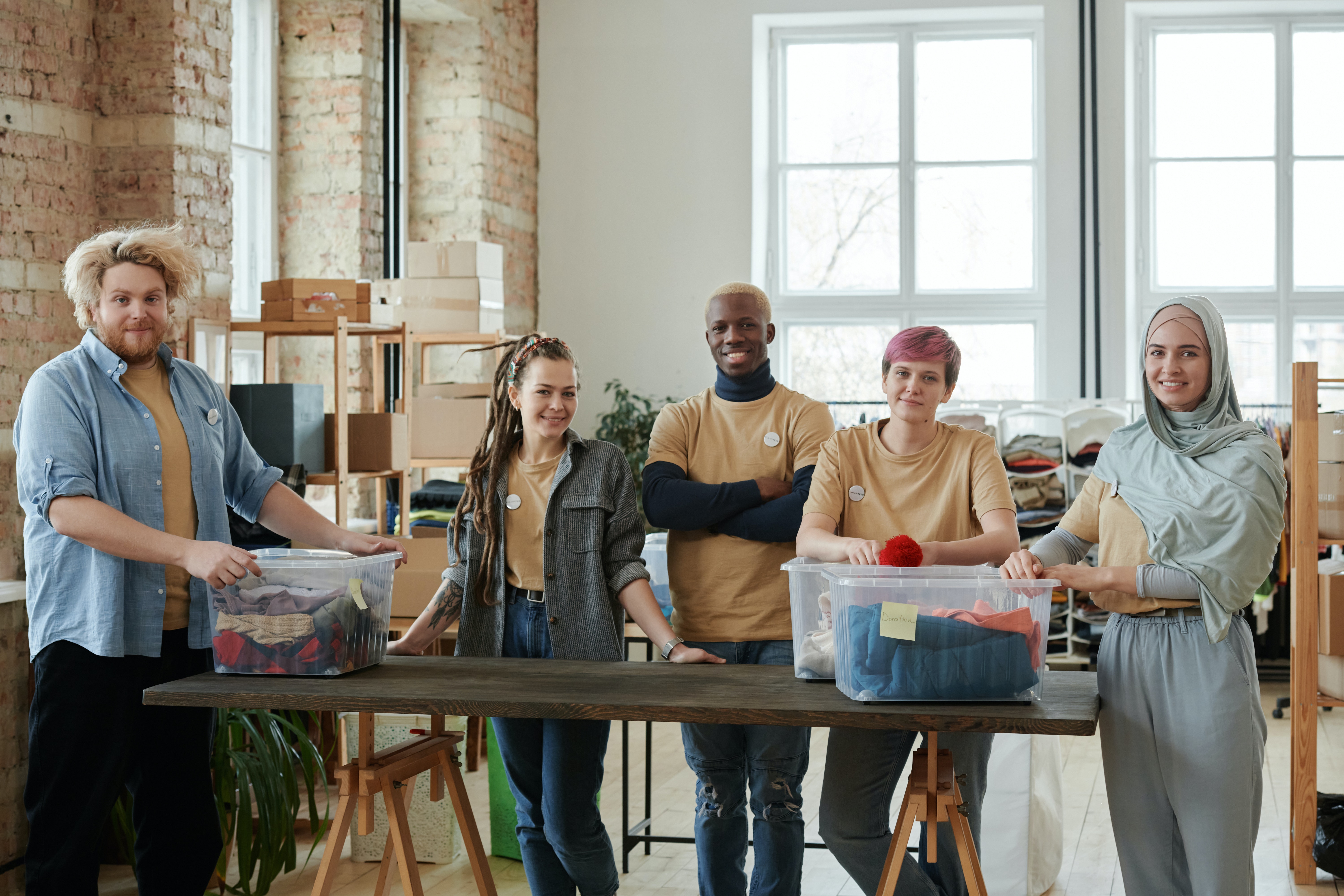 three people standing behind a table in all the same shirt, appearing to work at a clothing drive, this picture is used to represent nonprofits. 
