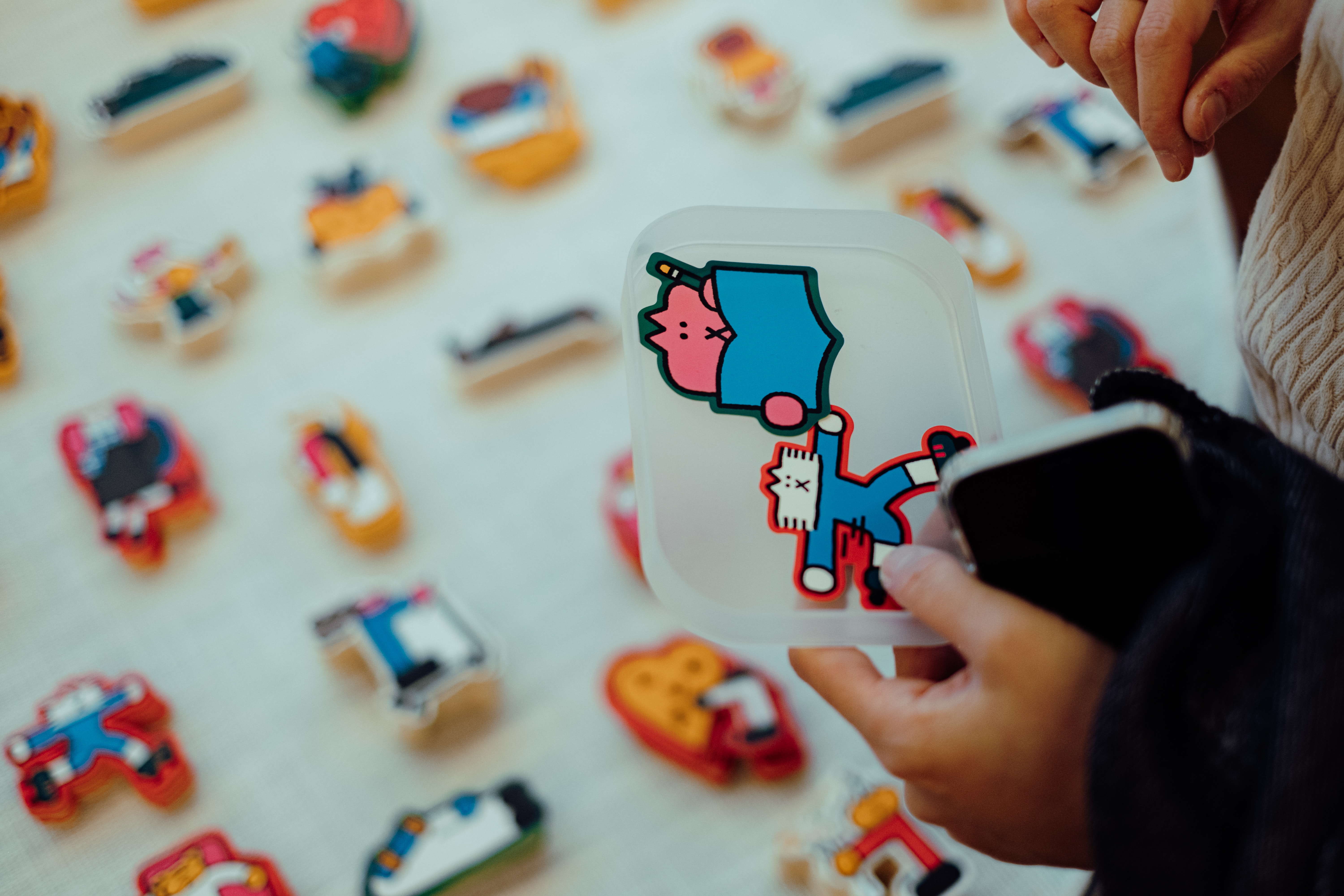 a person is holding a tray of with 2 stickers and it looks like they are colecting sticers for an order, as the rest of the picture is an out of focus table with at least a dozen stacks of stickers. 