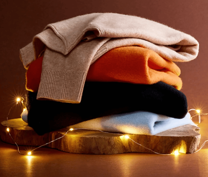 Sweaters stacked atop a tree stump slice, with a string of white lights circling the stump