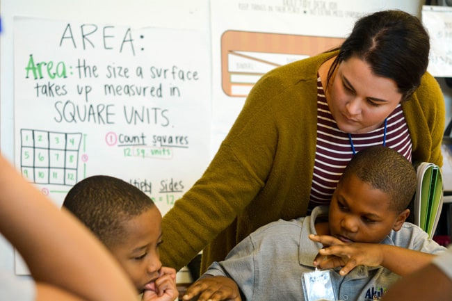 Teacher with students at a desk, helping them with their work.