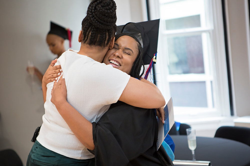 Relay graduate in cap and gown hugging a friend.