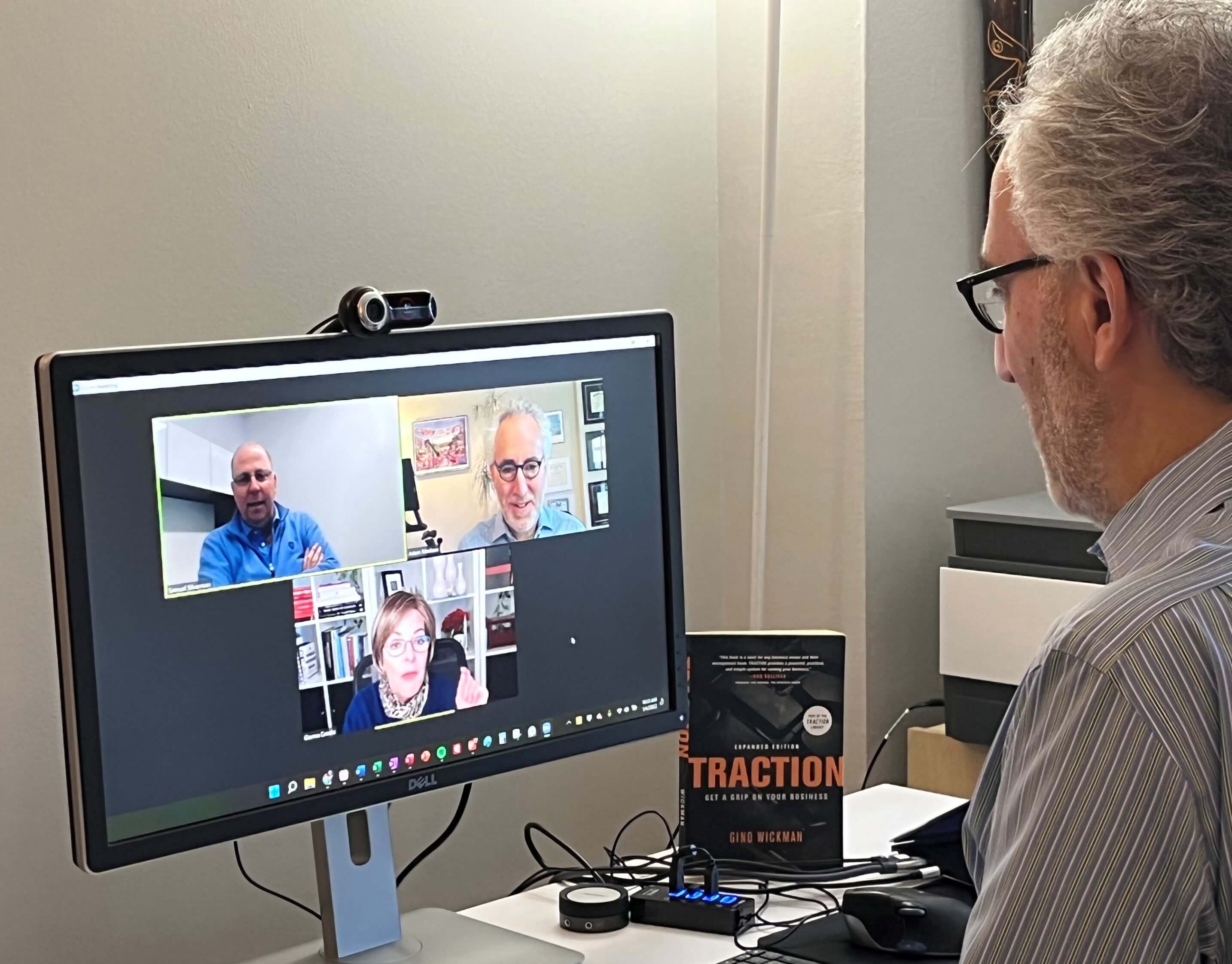 Monitor on a desk with a video Zoom call occurring and Adam in an office chair on the right.