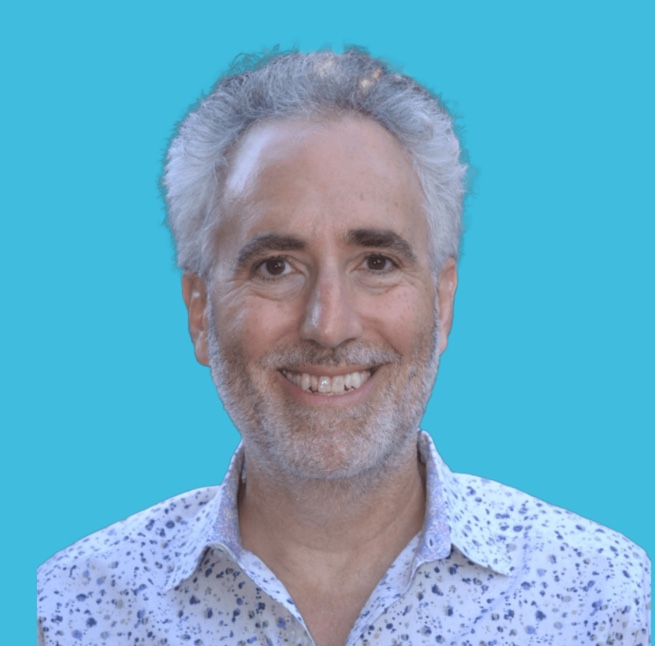 Headshot of man with gray and white hair in white button down shirt with a blue background.
