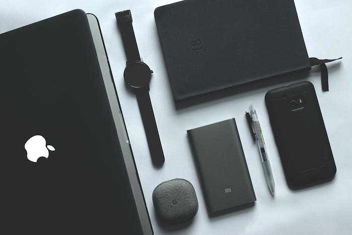 Un ordinateur portable, une montre, un disque dur, une enceinte et une tablette noirs, posés sur un fond blanc et vus du dessus témoignent de la pollution numérique.