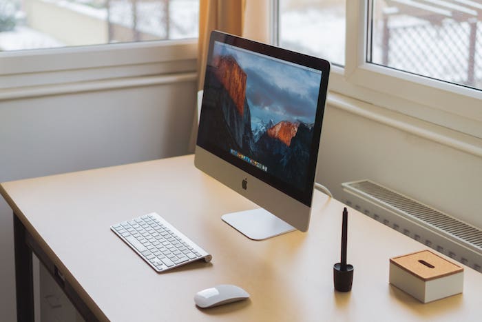 Ordinateur fixe grand écran posé sur une table en bois dans un bureau lumineux.