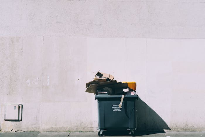 Poubelle noire dans la rue remplie de cartons qui débordent.