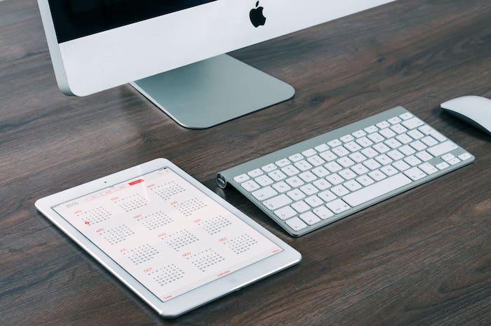 Différents outils informatiques posés sur une table en bois : un clavier, une souris, une tablette et un ordinateur fixe.