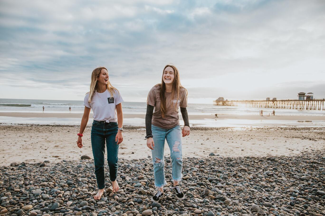Two girls walking side by side on a beach.