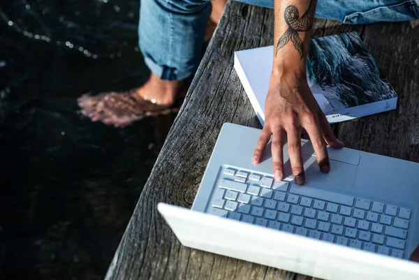 Une main d'homme tatoué et assis sur un banc , la main sur son ordinateur portable