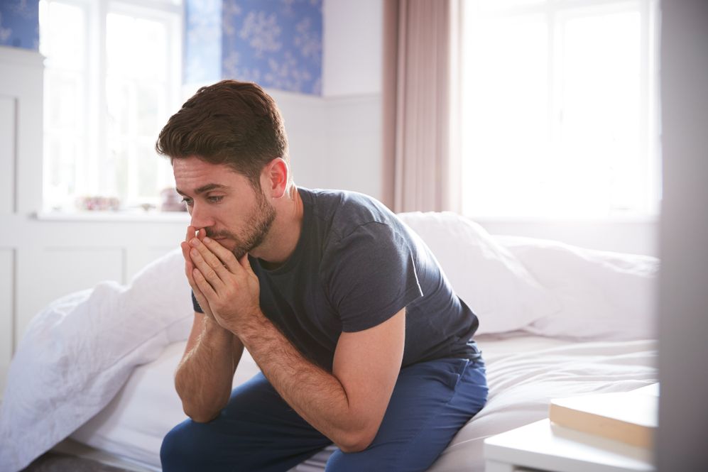 a problematic man who is addicted to xanax bar is sitting on a white bed and thinking deeply