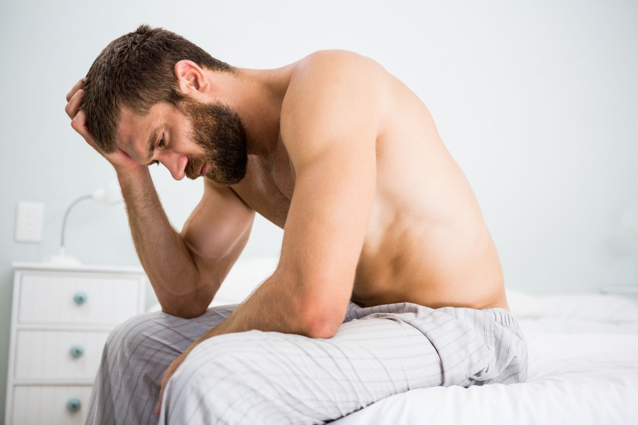 a man who is abusing adderall is seen here holding his head while sitting on a white bed