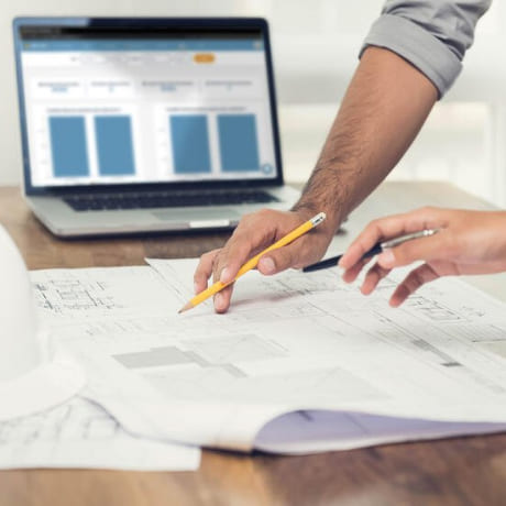 Main de deux personnes qui dessinent sur un plan de chantier