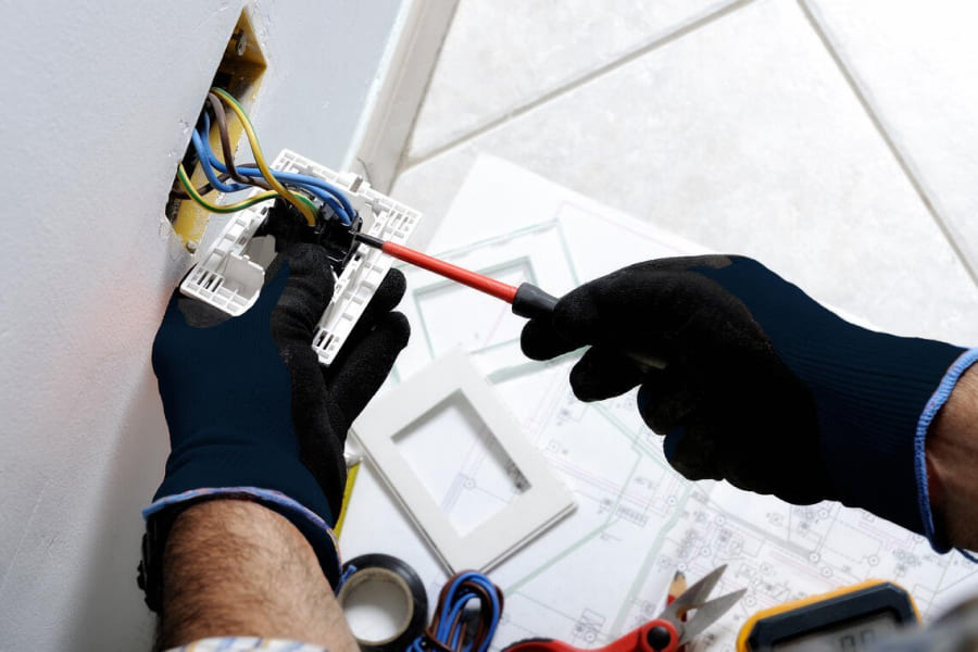 Mains d'un technicien qui répare une prise électrique avec un tourne vis
