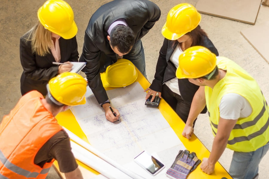 Réunion de chantier avec cinq personnes autour des plans d'un bâtiment