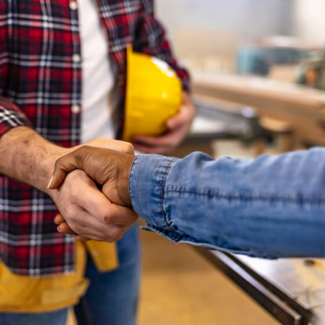Un artisan avec un casque de chantier dans la main qui fait une poignée de main à un client
