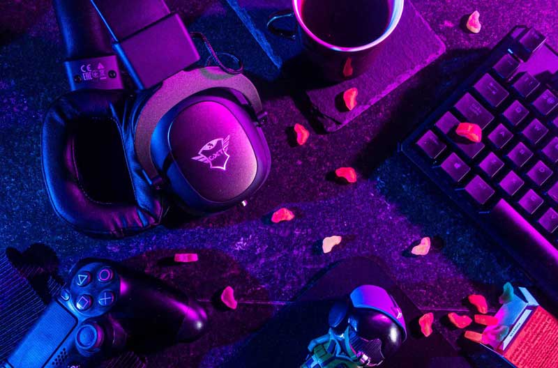 Top-view of a table with a keyboard, headphones, a gaming controller and a gaming mouse.